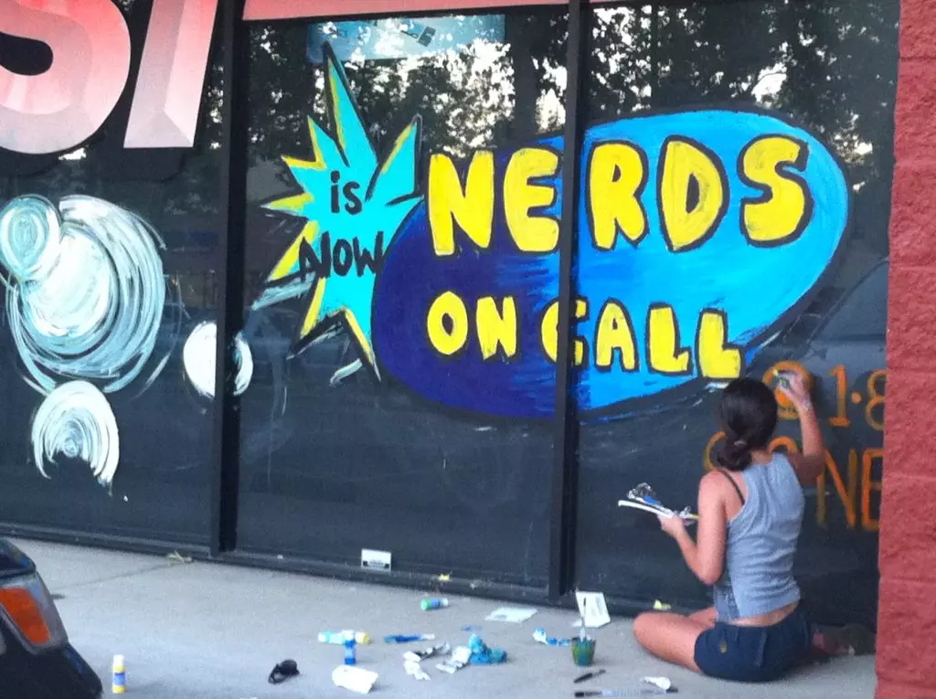 Woman painting Nerds On Call Logo on store front